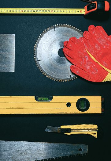 Outils de chantier : niveau, scie, mètre et gants de protection.